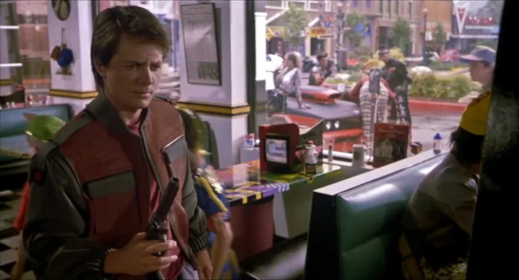 Fütüristik bir kafede içecek şişesi tutan Marty McFly